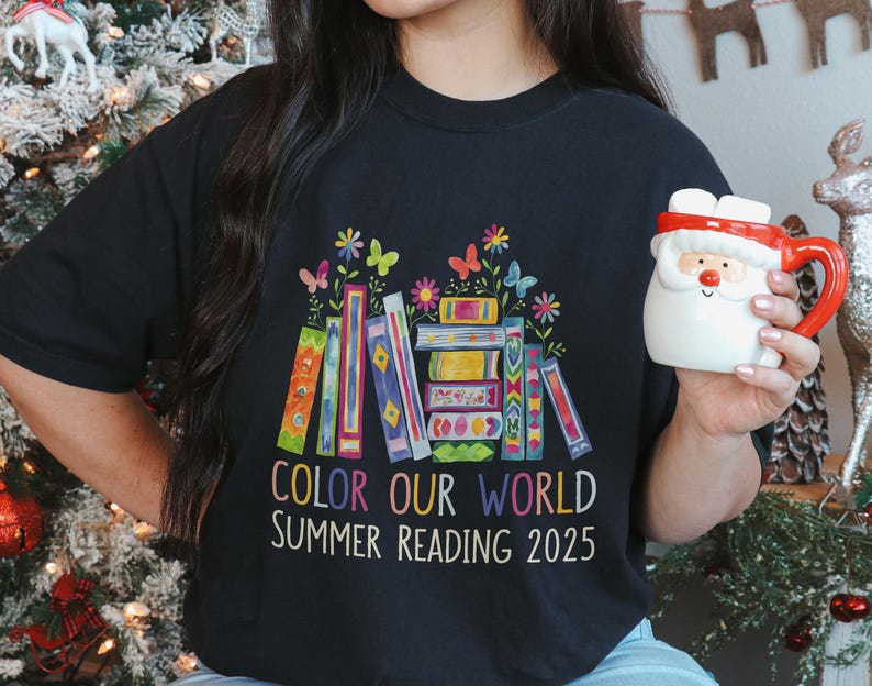 May include: Black t-shirt with a colorful illustration of stacked books and flowers. The text "Color Our World Summer Reading 2025" is printed on the shirt.
