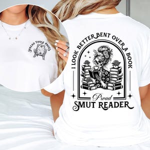May include: White t-shirt with a black and white graphic of a skeleton reading a book. The text on the shirt reads "I look better bent over a book. Proud smut reader."