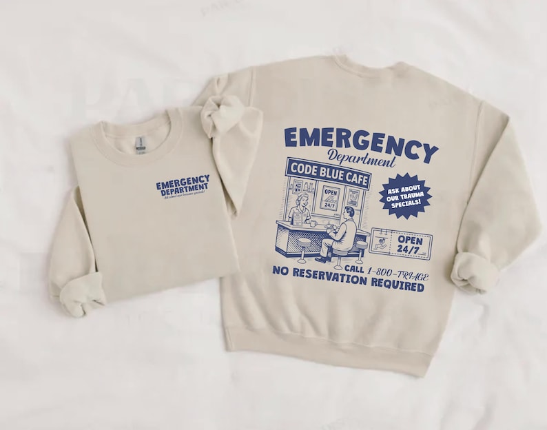 May include: Two beige sweatshirts. One has "EMERGENCY DEPARTMENT" printed on the front. The other has the same text on the front, and a graphic on the back that says "EMERGENCY Department CODE BLUE CAFE" with additional text and illustrations in blue.