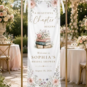 May include: A vertical white fabric banner hanging from a gold metal frame with white ribbons. It features floral illustrations, a stack of vintage books, and the text: A BEAUTIFUL Chapter BEGINS, Welcome to SOPHIA'S BRIDAL SHOWER, August 18, 2026.