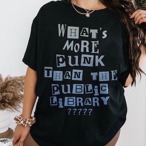 May include: Black t-shirt with the text "WHAT'S MORE PUNK THAN THE PUBLIC LIBRARY ?????" in a blue and white block letter design. The shirt has short sleeves and a crew neck.