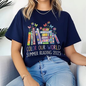 May include: A navy blue t-shirt with a colorful stack of books and butterflies. The text on the shirt reads "Color Our World Summer Reading 2025".