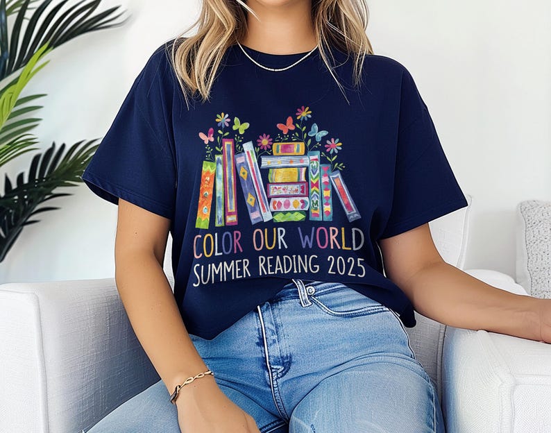 May include: A navy blue t-shirt with a colorful stack of books and butterflies. The text on the shirt reads "Color Our World Summer Reading 2025".