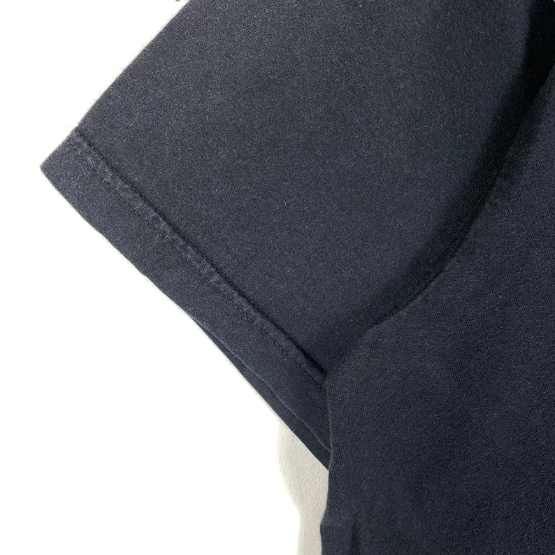 K&ouml;nnte beinhalten: Nahaufnahme des dunkelblauen Stoffes eines T-Shirt-&Auml;rmels. Der Stoff ist glatt und hat eine subtile Textur.