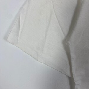 May include: Close-up of a white cotton t-shirt fabric, showing the texture and weave of the material.