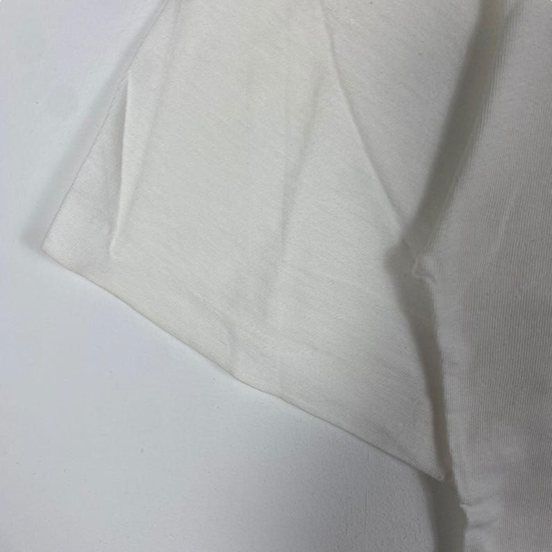 May include: Close-up of a white cotton t-shirt fabric, showing the texture and weave of the material.