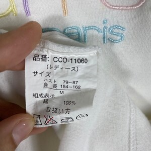 May include: White t-shirt with a colorful embroidered logo that says "Paris". The tag on the shirt says "CCO-11060 (Ladies)", "Size", "Bust 79-87", "Height 154-162", "M", "Composition: Cotton 100%", and "Care Instructions".