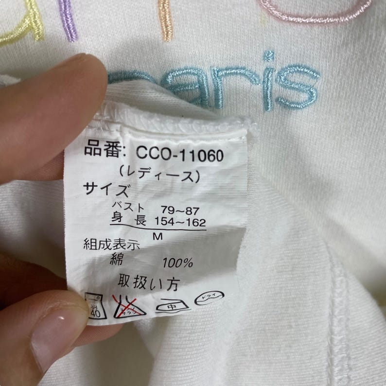 May include: White t-shirt with a colorful embroidered logo that says "Paris". The tag on the shirt says "CCO-11060 (Ladies)", "Size", "Bust 79-87", "Height 154-162", "M", "Composition: Cotton 100%", and "Care Instructions".