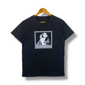 May include: Black t-shirt with a white graphic of a woman with a tattoo and the word " Utopia" printed below the image.