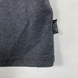 K&ouml;nnte beinhalten: Ein dunkelgraues geripptes T-Shirt mit einem schwarzen Etikett, auf dem rechts unten "SACSNY" steht.