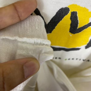 May include: Close-up of a white t-shirt with a black and yellow graphic design. The shirt has a tag with the word "M" on it.