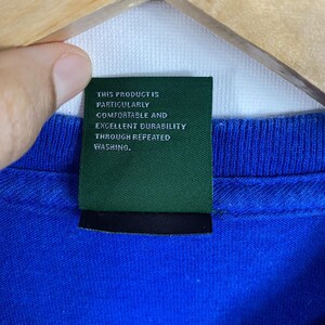 May include: A close-up of a blue t-shirt with a green tag that reads "This product is particularly comfortable and excellent durability through repeated washing."
