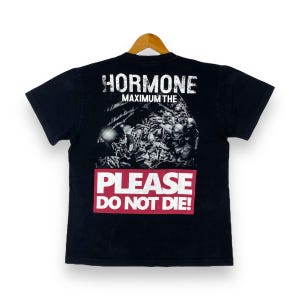 Puede incluir: Camiseta negra con un estampado gráfico blanco de un grupo de soldados. El texto "HORMONE MAXIMUM THE" y "PLEASE DO NOT DIE!" está impreso en la camiseta.