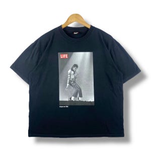 May include: Black t-shirt with a photo of Michael Jackson on the front. The photo is from a LIFE magazine cover. The text "LIFE" is in red letters above the photo. The text "Photo by DM" is below the photo.