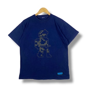 May include: A navy blue t-shirt with a pixelated graphic of a soldier holding a weapon. The graphic is in gray and black. The t-shirt has a small blue tag with the text "MM" on the bottom right corner.