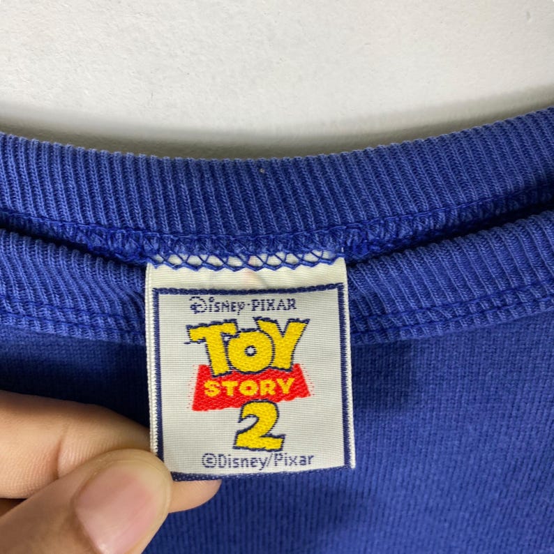 May include: A blue cotton t-shirt with a white tag that says "Disney Pixar Toy Story 2 &copy;Disney/Pixar".