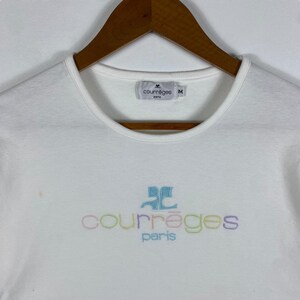 May include: White t-shirt with a colorful embroidered logo that says "Courr&egrave;ges Paris". The logo is in a rainbow of colors, including pink, blue, green, and yellow. The shirt has a crew neck and short sleeves. The tag on the shirt says "Courr&egrave;ges Paris" and "M".