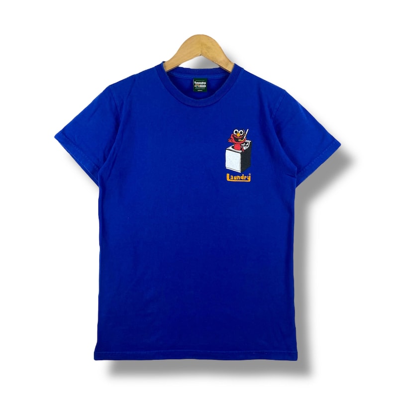 May include: A royal blue t-shirt featuring a graphic of Elmo in a washing machine. The text "Laundry" is printed below the graphic.
