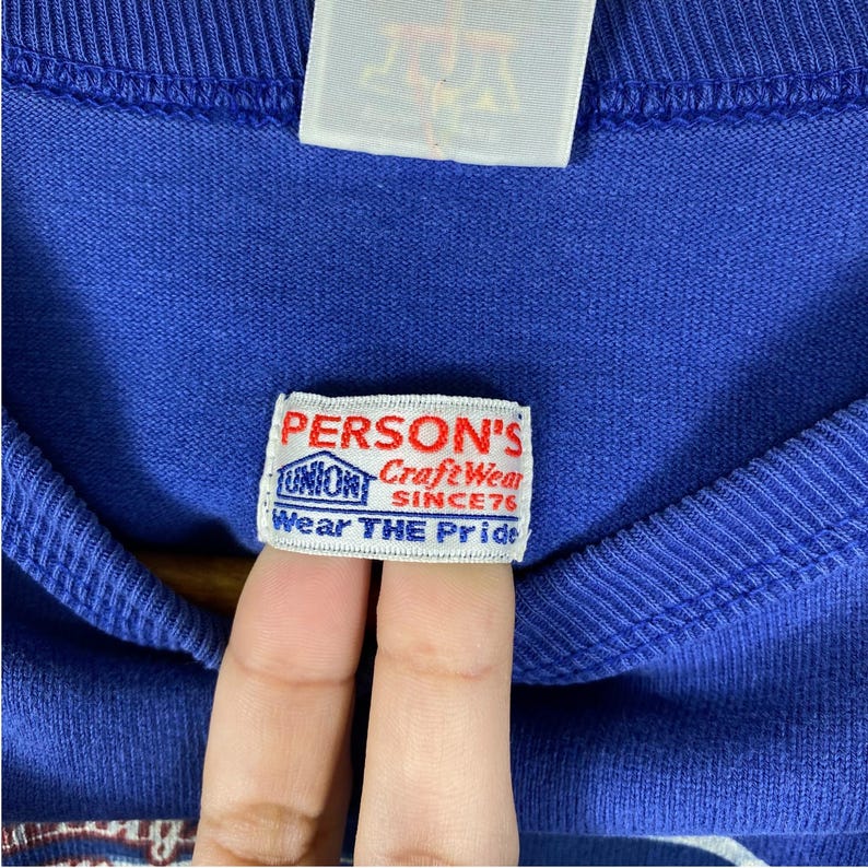 May include: A blue sweatshirt with a white label that reads "PERSON'S CraftWear SINCE'76 Wear THE Pride".