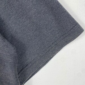 K&ouml;nnte beinhalten: Nahaufnahme des dunkelgrauen Stoffes eines T-Shirts. Der Stoff hat eine strukturierte, leicht gerippte Oberfl&auml;che.