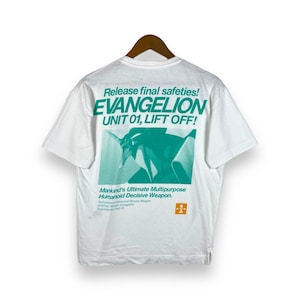 Peut inclure: T-shirt blanc avec un imprimé graphique vert et blanc d'un robot avec le texte "Release final safeties! EVANGELION UNIT 01, LIFT OFF!" et "Mankind's Ultimate Multipurpose Humanoid Decisive Weapon."