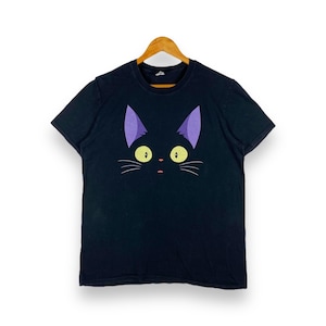 Puede incluir: Camiseta negra con un gráfico de cara de gato morado. El gato tiene ojos amarillos y una expresión de sorpresa.