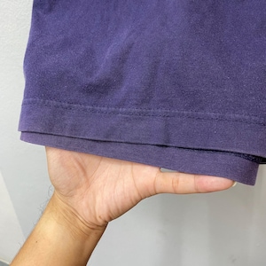 May include: Close-up of a deep purple t-shirt hem. The fabric appears soft and slightly worn, with a visible seam detail. The shirt is held by a hand, suggesting it's being displayed or examined. The overall impression is of a casual, everyday garment.