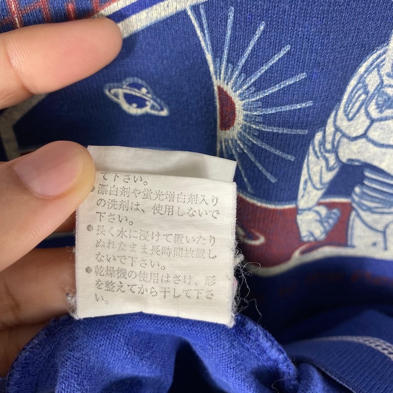 May include: A white care tag with black text on a blue background. The text reads: "Please do not use bleach or fluorescent whitening agents. Do not soak in water for long periods of time. Do not use a dryer. Please reshape and hang to dry."