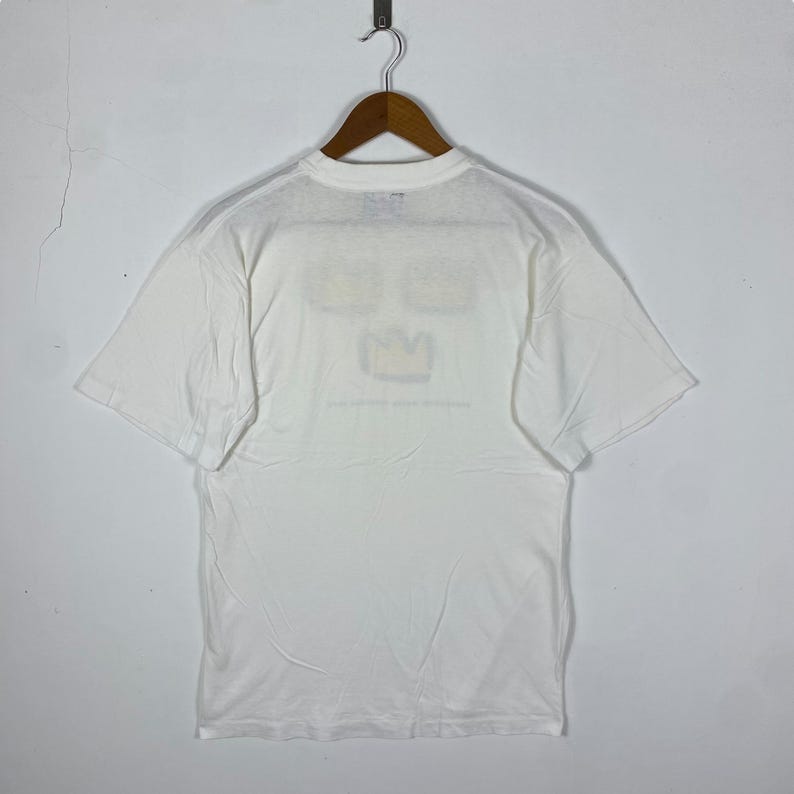 May include: White t-shirt with a graphic of three yellow crowns on the front. The graphic is a simple line drawing with a black outline.