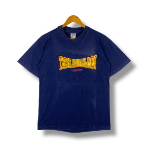 Puede incluir: Una camiseta azul marino con un gráfico amarillo y rojo que dice "These Animal Men London".