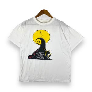 Puede incluir: Camiseta blanca con un gr&aacute;fico negro y amarillo de Jack Skellington de "Pesadilla antes de Navidad". El gr&aacute;fico muestra a Jack de pie en una colina con una luna detr&aacute;s de &eacute;l. El texto "Tim Burton's The Nightmare Before Christmas" est&aacute; impreso debajo del gr&aacute;fico.