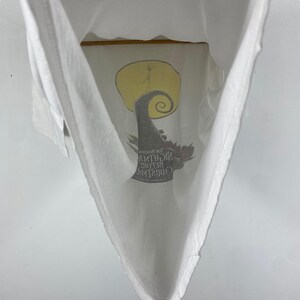 Puede incluir: Camiseta blanca con un estampado gr&aacute;fico de Jack Skellington de la pel&iacute;cula "Pesadilla antes de Navidad". El gr&aacute;fico muestra a Jack Skellington de pie en una colina con una luna llena detr&aacute;s de &eacute;l. El texto "Pesadilla antes de Navidad" est&aacute; impreso debajo del gr&aacute;fico.