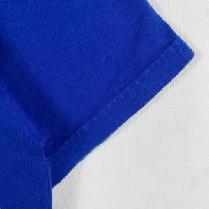 May include: Close-up of the blue fabric sleeve of a shirt. The fabric is smooth and has a subtle texture.