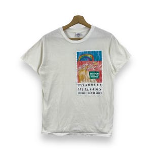 Puede incluir: Camiseta blanca con un estampado gráfico colorido de un arcoíris y una persona. El texto "Freedom from the known" y "Pharrell Williams World Tour 2015" está impreso en la camiseta.
