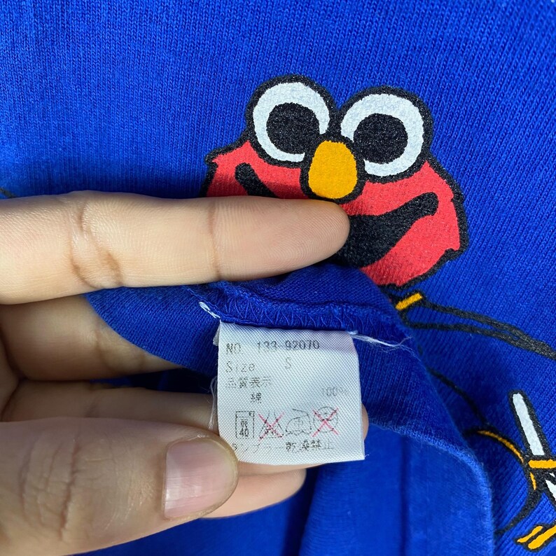 May include: Blue t-shirt featuring a red Elmo character graphic. The tag reads "NO. 133-92010 Size S".