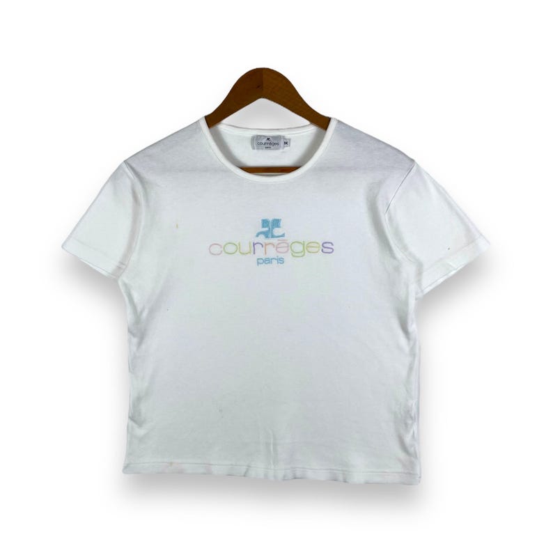 May include: White short-sleeved t-shirt with a colorful "Courr&egrave;ges Paris" logo embroidered on the front.
