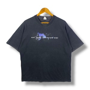 May include: Black t-shirt with the text "LET YOUR DARKSIDE OUT" in white. The graphic above the text features a blue and purple design. The shirt is hanging on a wooden hanger.