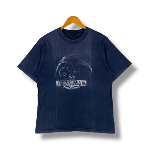 Op de afbeelding: Een marineblauw t-shirt met een witte afbeelding van een demon met de tekst "DEVILMAN" eronder.