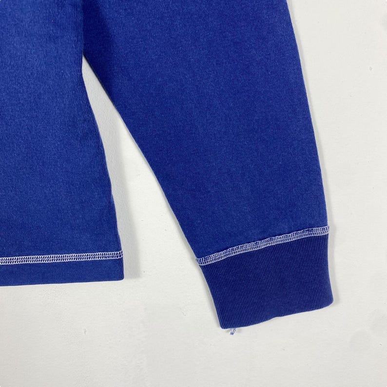 May include: A long-sleeved blue shirt with white stitching around the cuffs and hem.