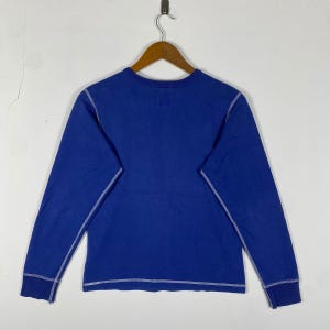 May include: A blue long-sleeved shirt with white stitching around the neckline, sleeves, and hem.
