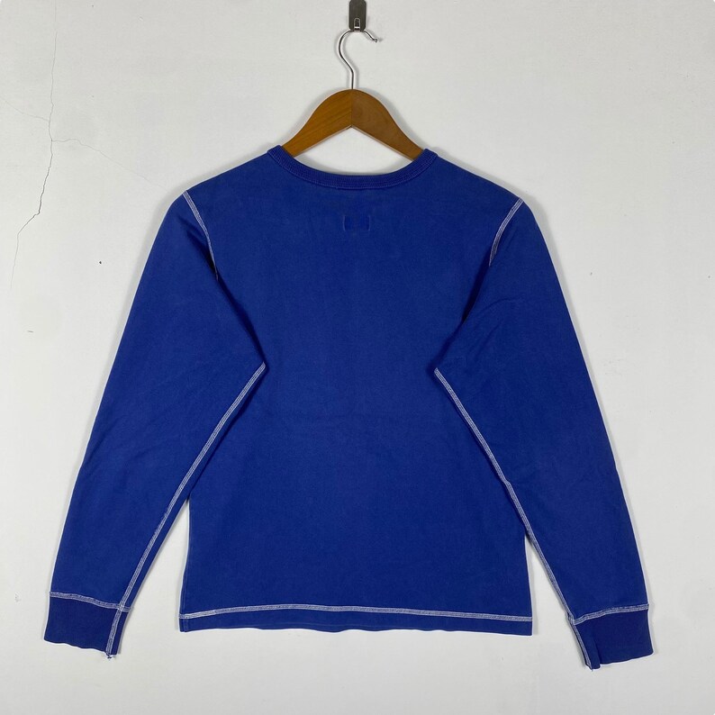 May include: A blue long-sleeved shirt with white stitching around the neckline, sleeves, and hem.