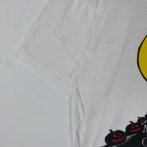 Puede incluir: Camiseta blanca con un gr&aacute;fico de cara sonriente negro y amarillo y un gr&aacute;fico de calabaza negro y rojo con el texto "Monster Mash"
