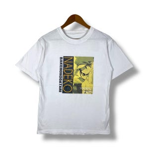 May include: White t-shirt with a yellow and black graphic print of a character from the anime series "Bakemonogatari". The text "Nadeko" and "Bakemonogatari" are printed on the shirt.