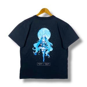 May include: Black t-shirt featuring a vibrant anime-style illustration of a character with long blue hair, set against a full moon and starry background. The design includes the text "OSAKA" and "TOKYO".