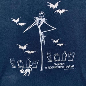 Puede incluir: Camiseta azul marino con un gr&aacute;fico blanco de Jack Skellington de "Pesadilla antes de Navidad" de Tim Burton. El dise&ntilde;o incluye murci&eacute;lagos, l&aacute;pidas y un gato. Tambi&eacute;n se ve el texto "Tim Burton's The Nightmare Before Christmas".