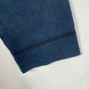 Puede incluir: Primer plano de una manga de tela azul marino. La manga tiene una textura acanalada y un dobladillo cosido en azul oscuro. La tela parece ser un tejido de peso medio, posiblemente algod&oacute;n o una mezcla de algod&oacute;n.