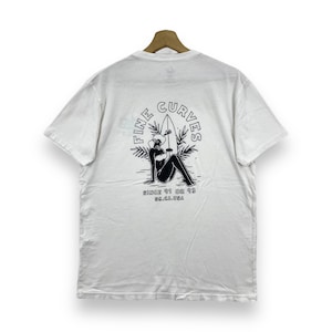 May include: White t-shirt with a black and white graphic print of a woman sitting on a surfboard with the text "Fine Curves" and "Since 91 or 93, So. Ca. USA."