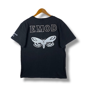 May include: Black t-shirt featuring a white moth design and the word "EMOD" on the back. The garment is displayed on a wooden hanger. The left sleeve has the words "Moth and" printed on it.