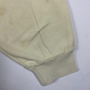 May include: Close-up of a pale yellow fabric sleeve with a ribbed cuff. The fabric has a textured appearance and shows several brown stains. The sleeve is slightly wrinkled.