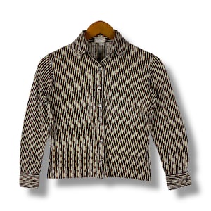 Puede incluir: Una camisa de manga larga con botones, de rayas marrones y crema, con cuello. La camisa tiene un patrón geométrico sutil y el nombre de la marca "CELINE" es visible en el cuello.